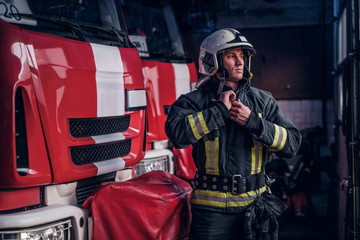 Fireman clothes protective uniforms standing next to the fire engine in the garage of a fire department