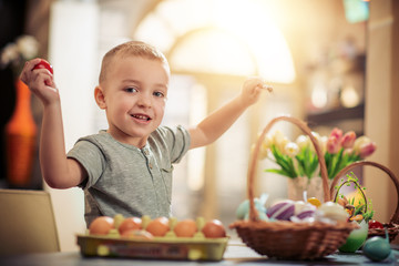 Happy child paints eggs for Easter at home