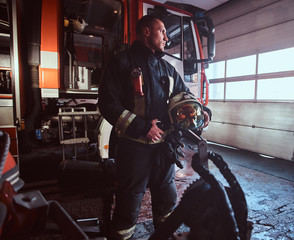 Handsome fireman wearing uniform looking outside while standing near a fire truck in a garage of a fire department