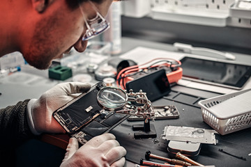 The technician uses a magnifying glass to carefully inspect the internal parts of the smartphone in...
