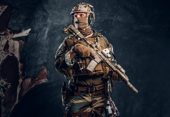 Fototapeta na wymiar Elite unit, special forces soldier in camouflage uniform posing with assault rifle. Studio photo against a dark textured wall