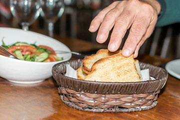 Golden toasts in a wicker basket for bread on a wooden rustic table. Male hand taking a piece of bread
