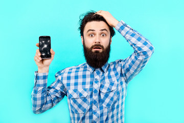 upset bearded man at a loss with broken mobile phones on a blue background, search concept gsm service
