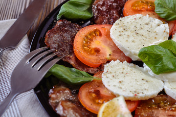 Appetizing salad with slices of tomatoes and mozzarella cheese, thin slices of roast beef and leaves of green basil, seasoned with oil and spices, closeup