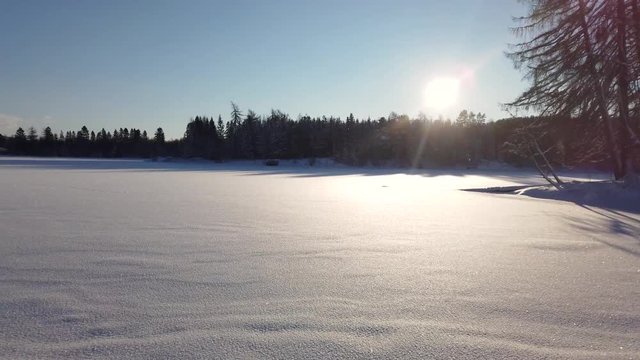 Pan over frozen lake, snow in air, sunny winter day.