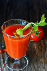 Fresh tomato juice in a glass goblet with a celery sprig and a tomato twig in the background in a low key