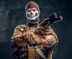 A terrorist in a military uniform and a skull balaclava holding a pistol and a knife and looks at...