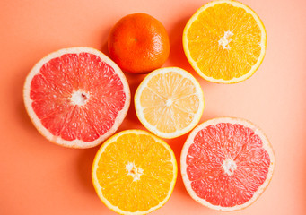 Flat lay of cut ripe juicy grapefruit, lemon and orange on orange color background. Citrus pattern.