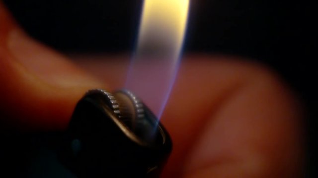man is lighting gas lighter in hand in darkness, sparks are flying, close-up view