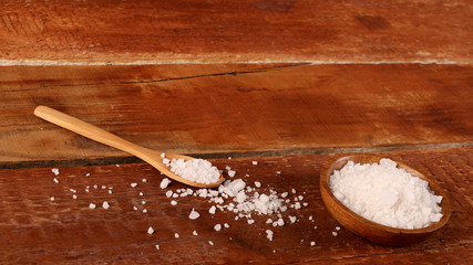 Salt or sea salt in a wooden bowl on a aged wooden table background.
