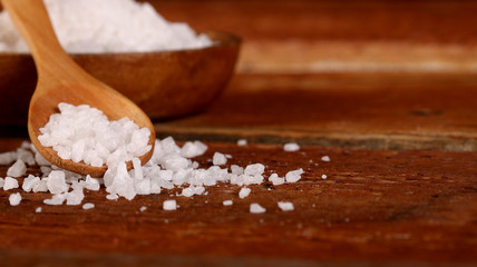 Salt or sea salt in a wooden bowl on a aged wooden table background.