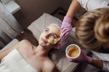 Cosmetologist doing beauty procedure for patient. Peeling Gold Mask