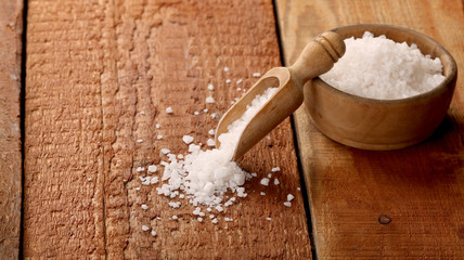Salt or sea salt in a wooden bowl on a aged wooden table background.