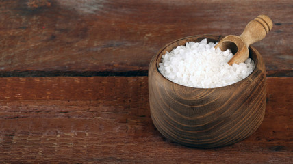 Salt or sea salt in a wooden bowl on a aged wooden table background.