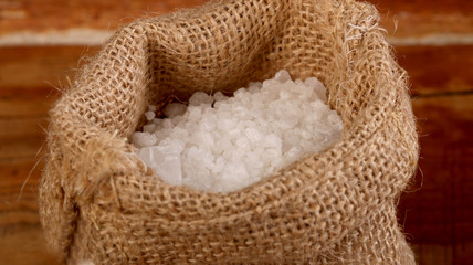 Obraz premium Salt or sea salt in a wooden bowl, burlap sack, bag and scoop on a aged wooden table background.