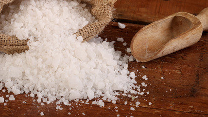 Salt or sea salt in a wooden bowl, burlap sack, bag and scoop on a aged wooden table background.
