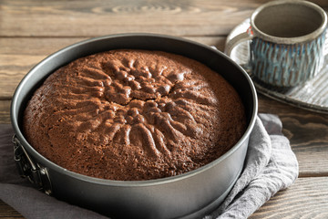 Freshly baked delicious smelling chocolate cake cools down in culinary form on a wooden table