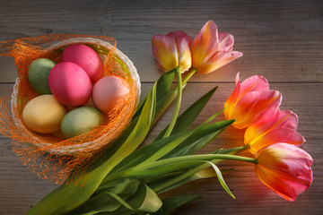 Multi-colored Easter eggs in a beautiful basket and a bouquet of tulips.