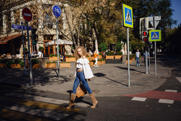 A beautiful young woman with blond curly hair walks through the sunny city