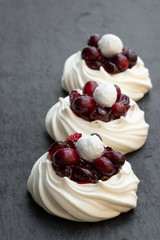 Mini Pavlova meringue nests with fresh and sugared cranberry on black stone background