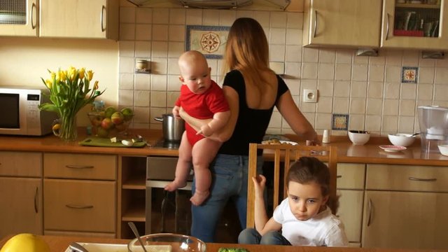 A young housewife with a baby in her arms feeds a preschool daughter. Mom with two children. Mothers Day