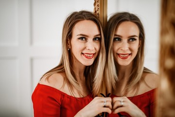 Beautiful girl in a red dress and glasses posing in the mirror.