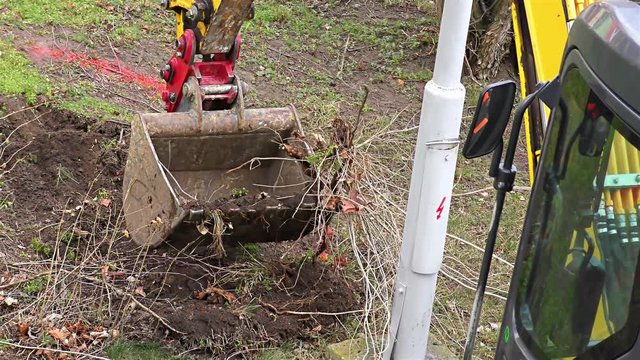 A Small Yellow Excavator Works Near the Building &ndash;  Excavator Loading Soil and Roots.