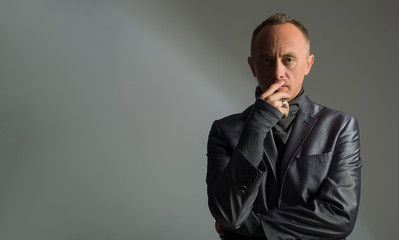 Model tests for men. A confident look to the frame and the hand touches the face. Gray background with shadow pattern. Confident and thoughtful man in a suit.