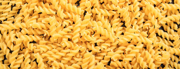 Uncooked fusilli spiral shape pasta texture background, banner