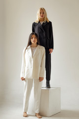 two women model posing for a photo. The blonde is dressed in a black suit and the brunette is dressed in a white suit. Stylish photo for advertising showroom or women's clothing store
