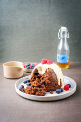 Traditional Australian plum pudding as closeup with fruits and vanilla rum sauce on a dessert plate with copy space