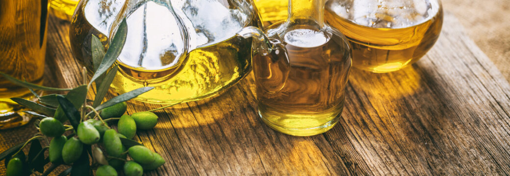 Olive oil in glass bottles on wooden table, banner, closeup view