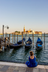 Fototapeta na wymiar Lady staring at Gondolas moored by Saint Mark square with San Giorgio di Maggiore church in the background in Venice, Italy