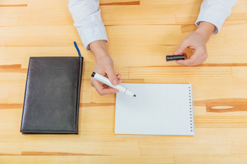 Black notebook with a white handle on the table top view. At the office desk is a black notebook. Female hands open the marker.