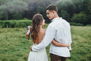 Happy wedding couple. Bride and groom embracing in the park. Autumn day. Woman holding her shoes on hand.