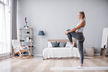 Full length portrait of attractive young woman working out at home, doing pilates exercise on mat.
