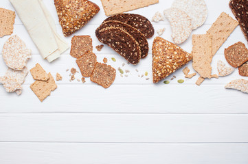 Various types of whole grain bread and crispbreads on white wooden background
