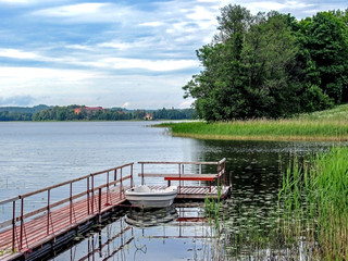 Obraz premium Small boat near wooden pier on the lake with green forest on the background