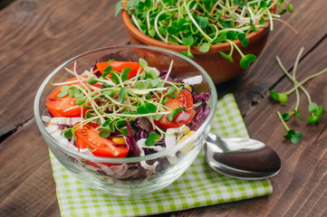 Salad with red cabbage, radish sprouts, corn and tomatoes on rustic wooden background