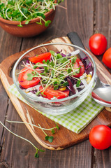 Salad with red cabbage, radish sprouts, corn and tomatoes on rustic wooden background
