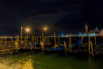Plakat Gondolas moored by Saint Mark square with San Giorgio di Maggiore church in the background in Venice, Italy at night
