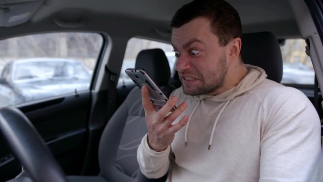 eccentric angry man is screaming and swearing on mobile phone, sitting in automobile on parking area