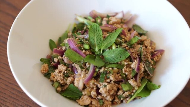 Homemade healthy Thai food Spicy Minced Pork Salad or called Larb Moo in white plate on brown table