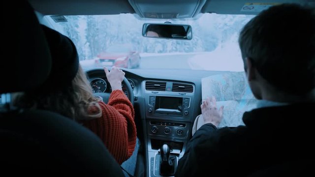 Shot from back of car on young couple drive through magical dreamy winter forest road.Woman drives and boyfriend studies vintage paper map to look for directions. Road trip travel wanderlust lifestyle - Powered by Adobe
