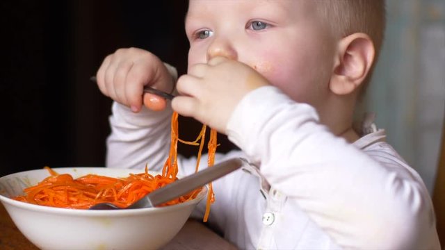 funny blond boy is eating Korean carrot salad in kitchen next to his brother. Children are happy together