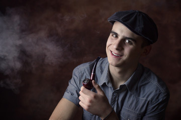 Closeup portrait of young man with beret hat, smoking a tobacco pipe and smiling. Thinking about something. Human facial expression, emotion, feeling, sign symbol body language