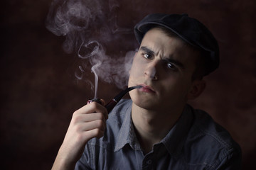 Closeup portrait of young man with beret hat, smoking a tobacco pipe. Very serious face expression. Human facial expression, emotion, feeling, sign symbol body language
