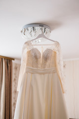 Very beautiful wedding dress of the bride hanging on the chandelier in the room.