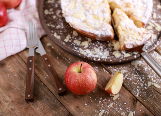 homemade apple pie on a plate with fresh apples and cinnamon sticks on a rustic wooden table