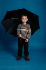 A little boy is standing under an open umbrella and smiling.